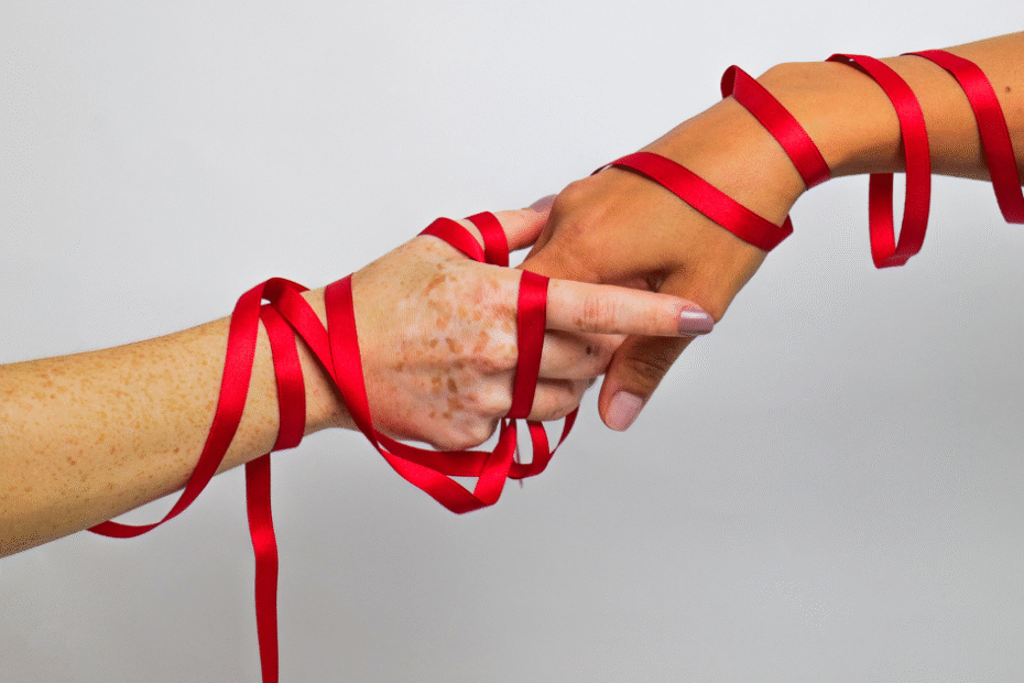 Mãos entrelaçadas com fita vermelha simbolizando a prevenção do HIV e a solidariedade na luta contra a AIDS