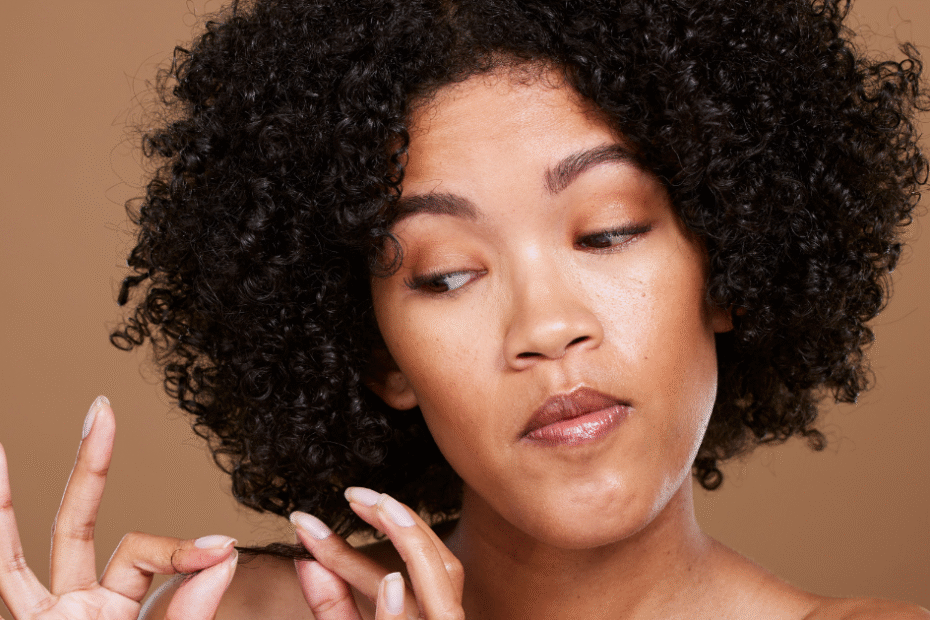 Mulher negra analisando o cabelo, representando a busca por vitaminas para fortalecimento dos fios.