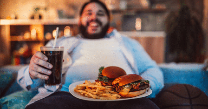 Homem comendo hambúrguer, batata frita e refrigerante, hábitos ligados à resistência insulínica e inflamação silenciosa