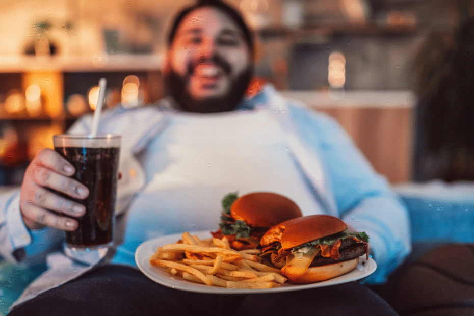 Homem comendo hambúrguer, batata frita e refrigerante, hábitos ligados à resistência insulínica e inflamação silenciosa